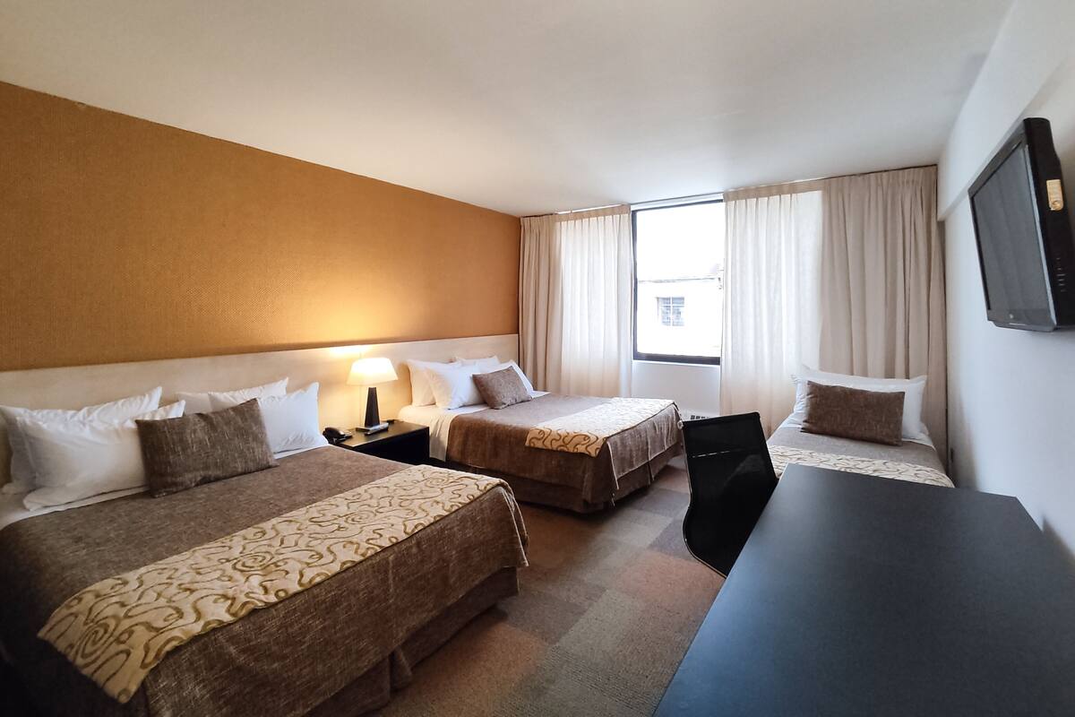 Una habitación de hotel con dos camas, un escritorio, un televisor y una ventana con cortinas.