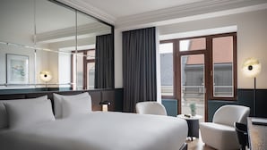 A hotel room with a large bed, a desk, a chair, a small table, a lamp, and a window with curtains.