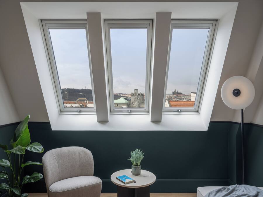 A room with a skylight, a chair, a small table with a plant, and a lamp.
