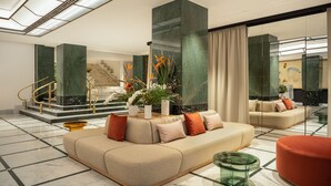 A modern lobby with a beige sofa, a glass coffee table, and a staircase with a golden railing.