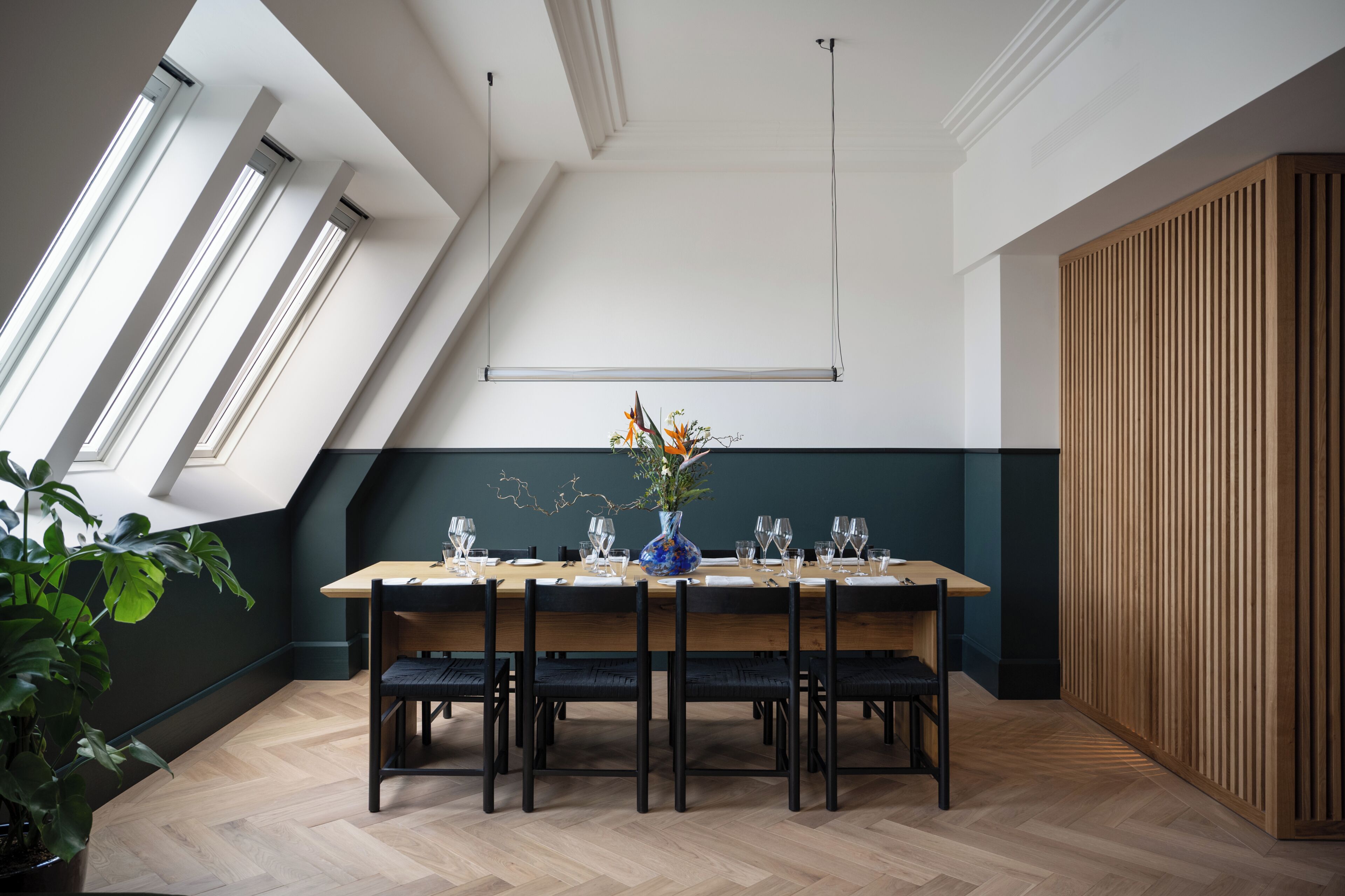 A dining area with a long table, chairs, a vase with flowers, and a wooden partition.