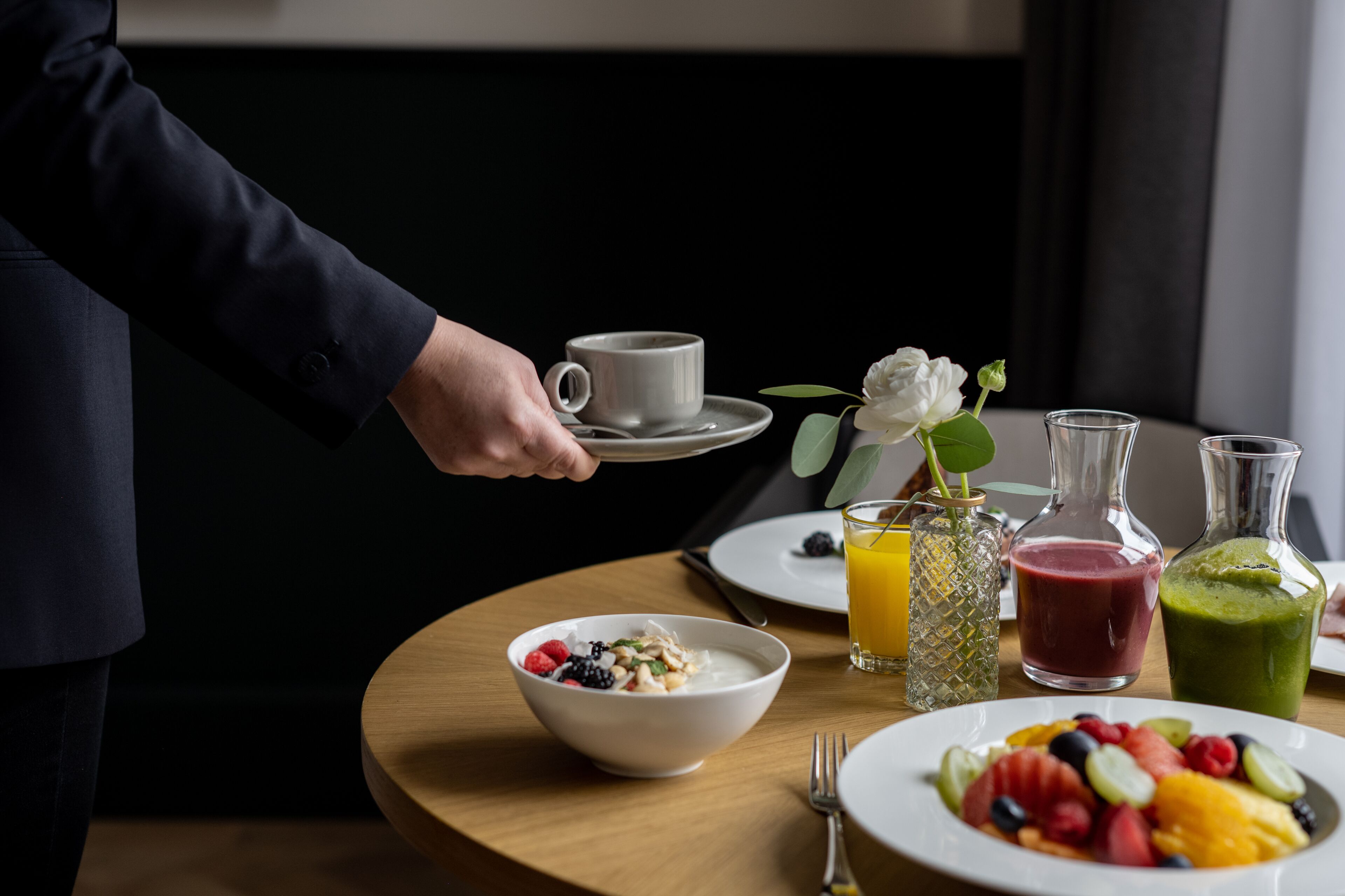 A breakfast setting with a bowl of cereal, a plate of fruit, and two glasses of juice on a wooden table.