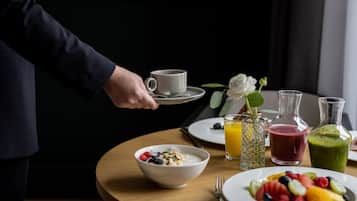 A breakfast setting with a bowl of cereal, a plate of fruit, and two glasses of juice on a wooden table.
