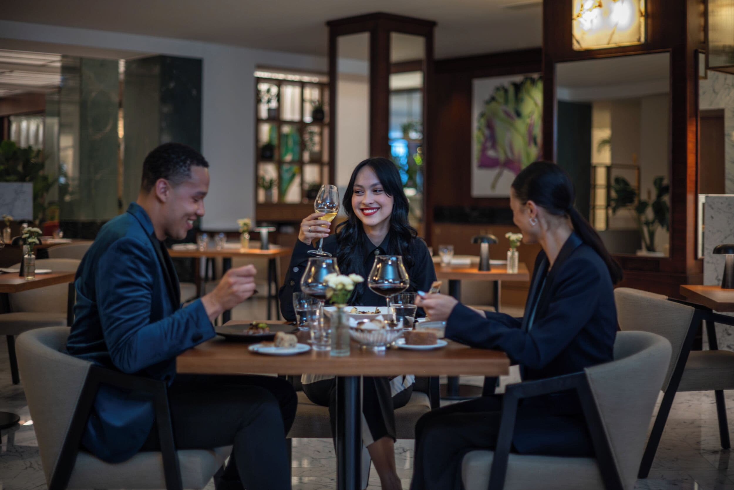 A group of people dining at a restaurant with a modern interior, including a chandelier and a large window.