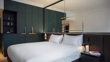 A modern bedroom with a large bed, dark green wardrobe, and a nightstand with a lamp and books.
