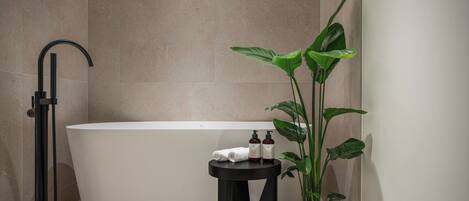 Une salle de bain moderne avec une baignoire sur pieds, un lavabo sur colonne noir et une plante en pot.