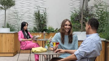 A wooden deck with three people seated at a table, one person reading a book, and another holding a drink.