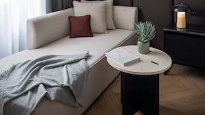 A modern hotel room with a sofa, a round side table, a mirror, and a potted plant.