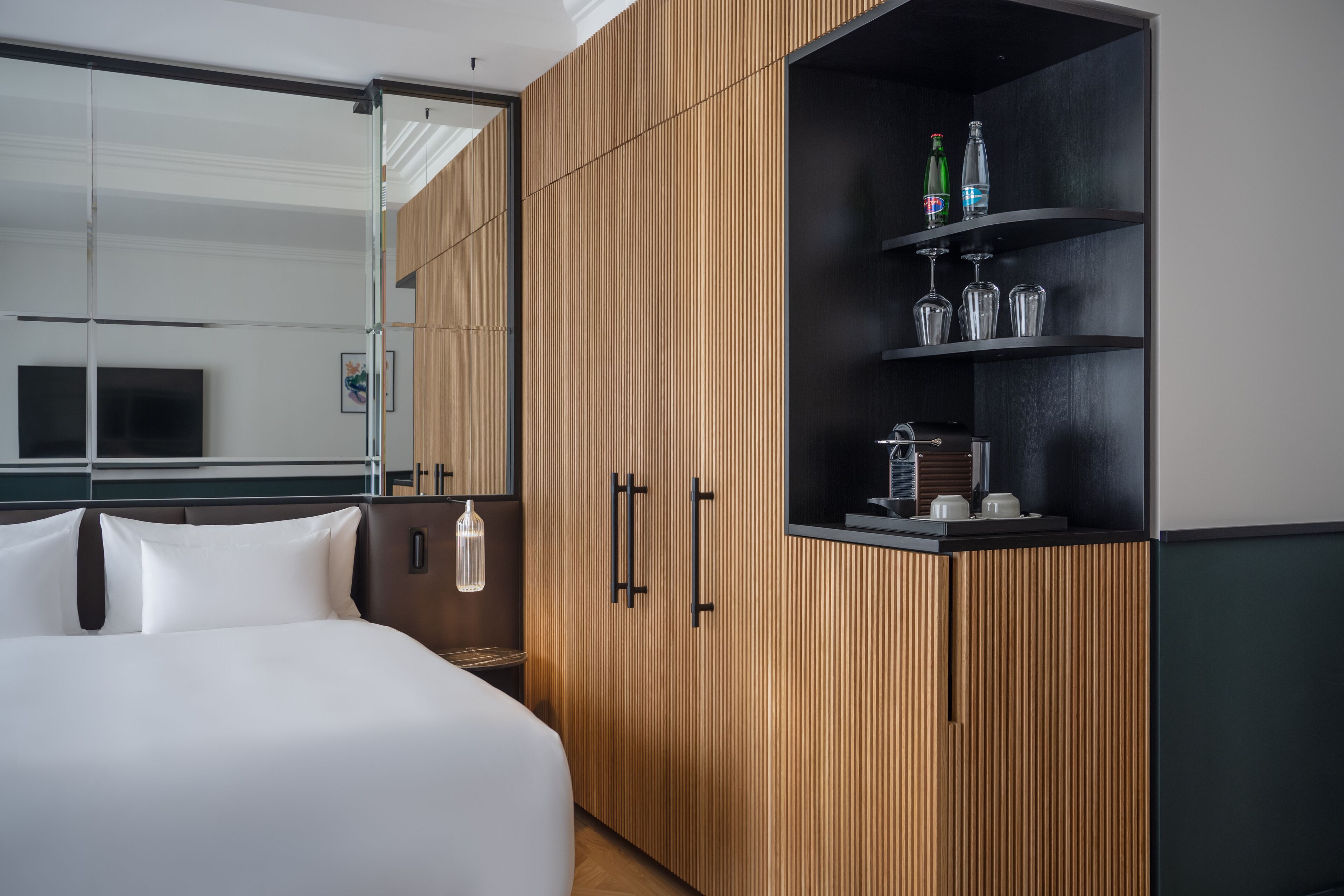 Een moderne hotelkamer met een groot bed, een houten kledingkast, een minibar en een televisie.