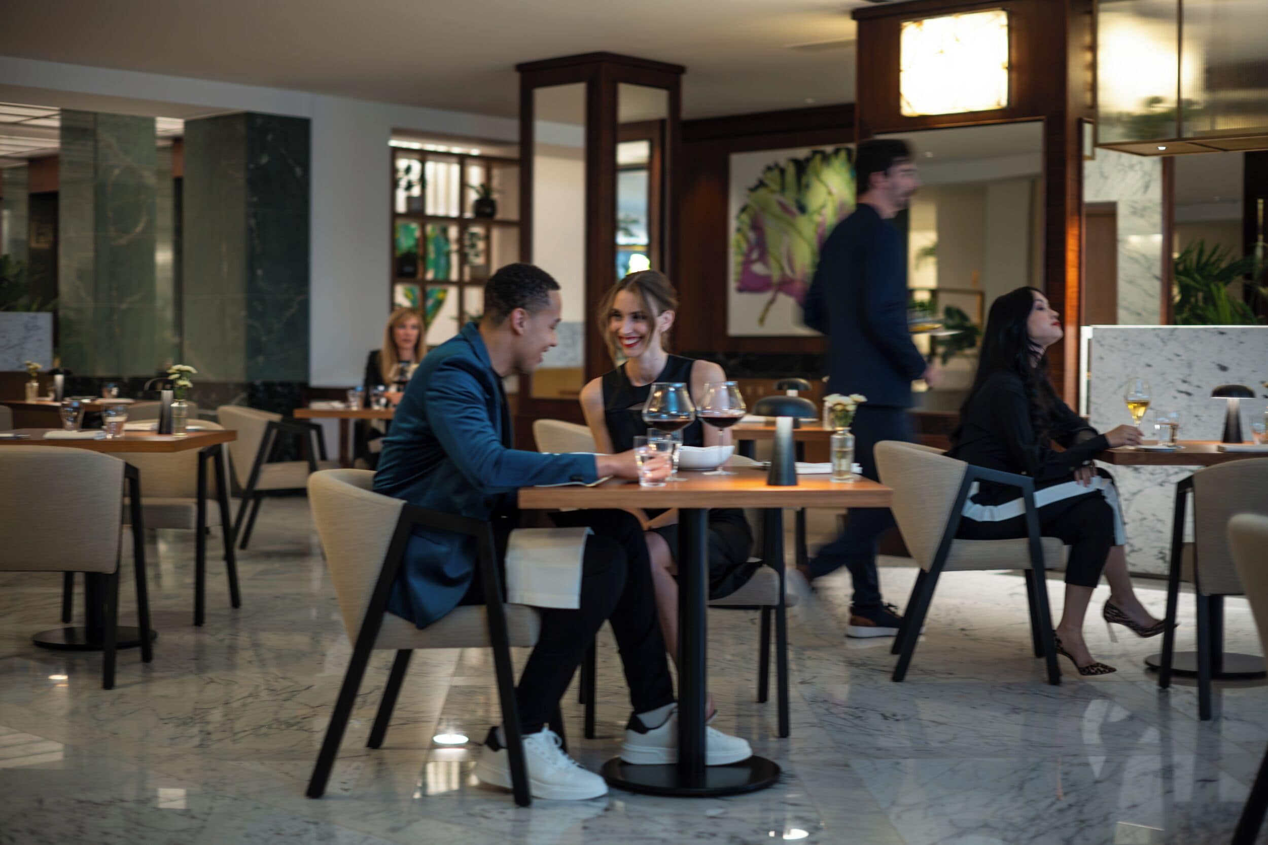 Un hall d’hôtel moderne avec un sol en marbre, des meubles en bois et un grand tableau accroché au mur.