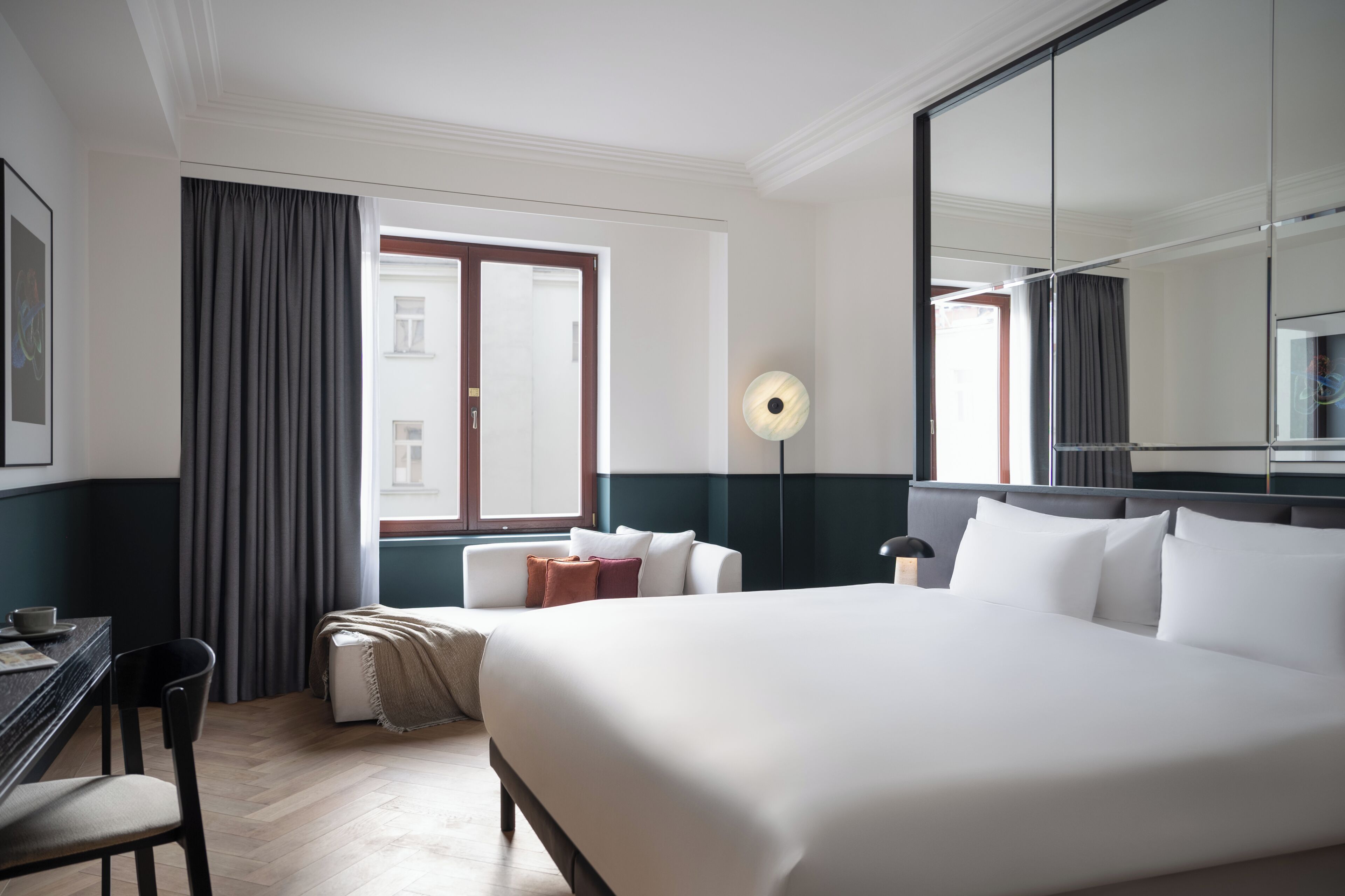Habitación de hotel con una cama grande, un escritorio, una silla, una lámpara y una ventana con cortinas.