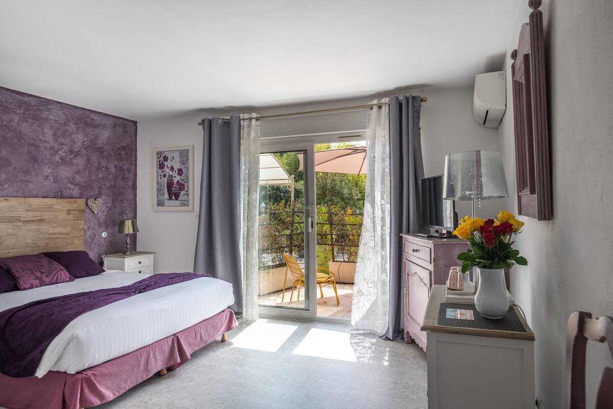 Ein Schlafzimmer mit einem Bett, einem Schreibtisch, einem Stuhl, einer Vase mit Blumen und einer Schiebetür zu einem Außenbereich.