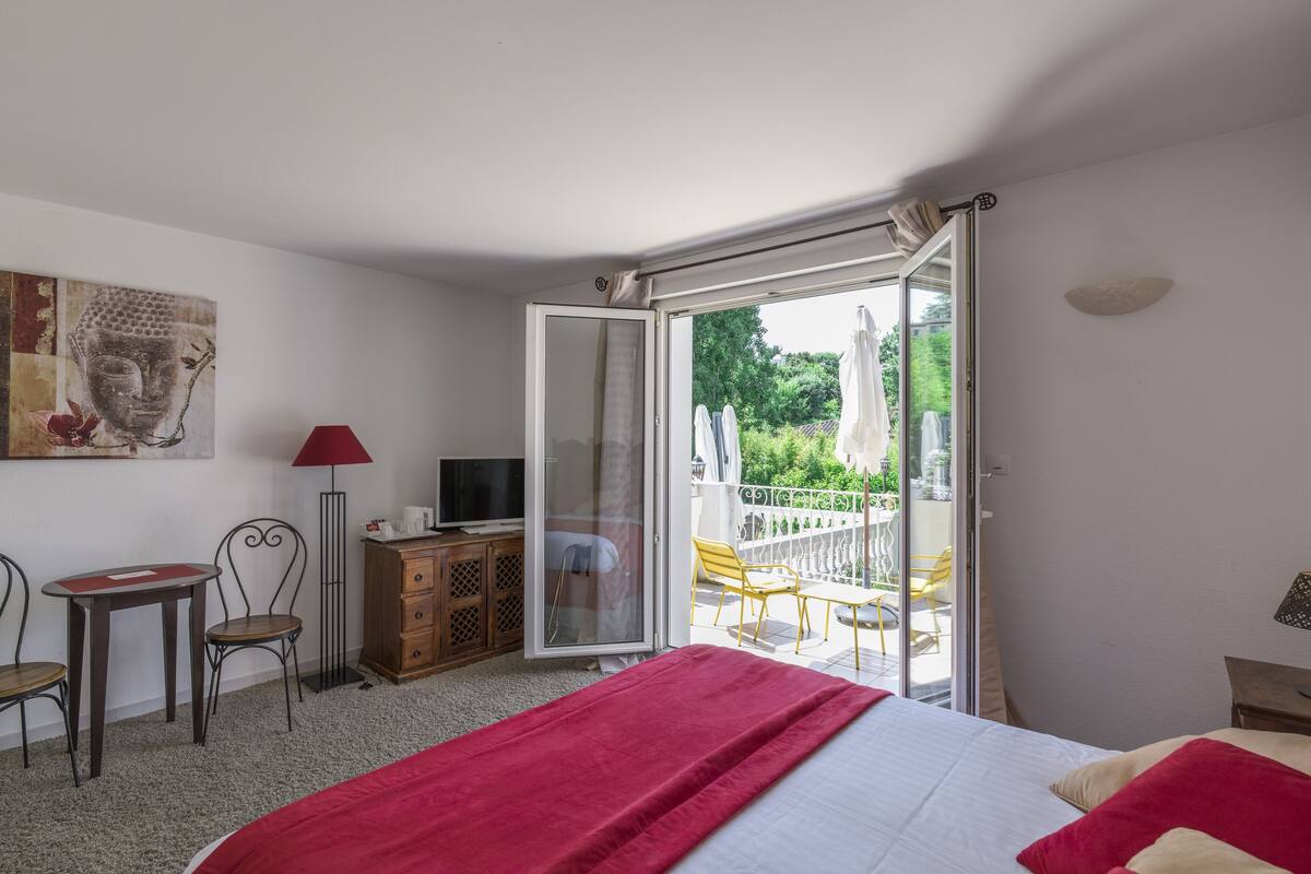 Ein Schlafzimmer mit Bett, Schreibtisch, Stuhl, Fernseher und einem Balkon mit Sitzmöbeln.