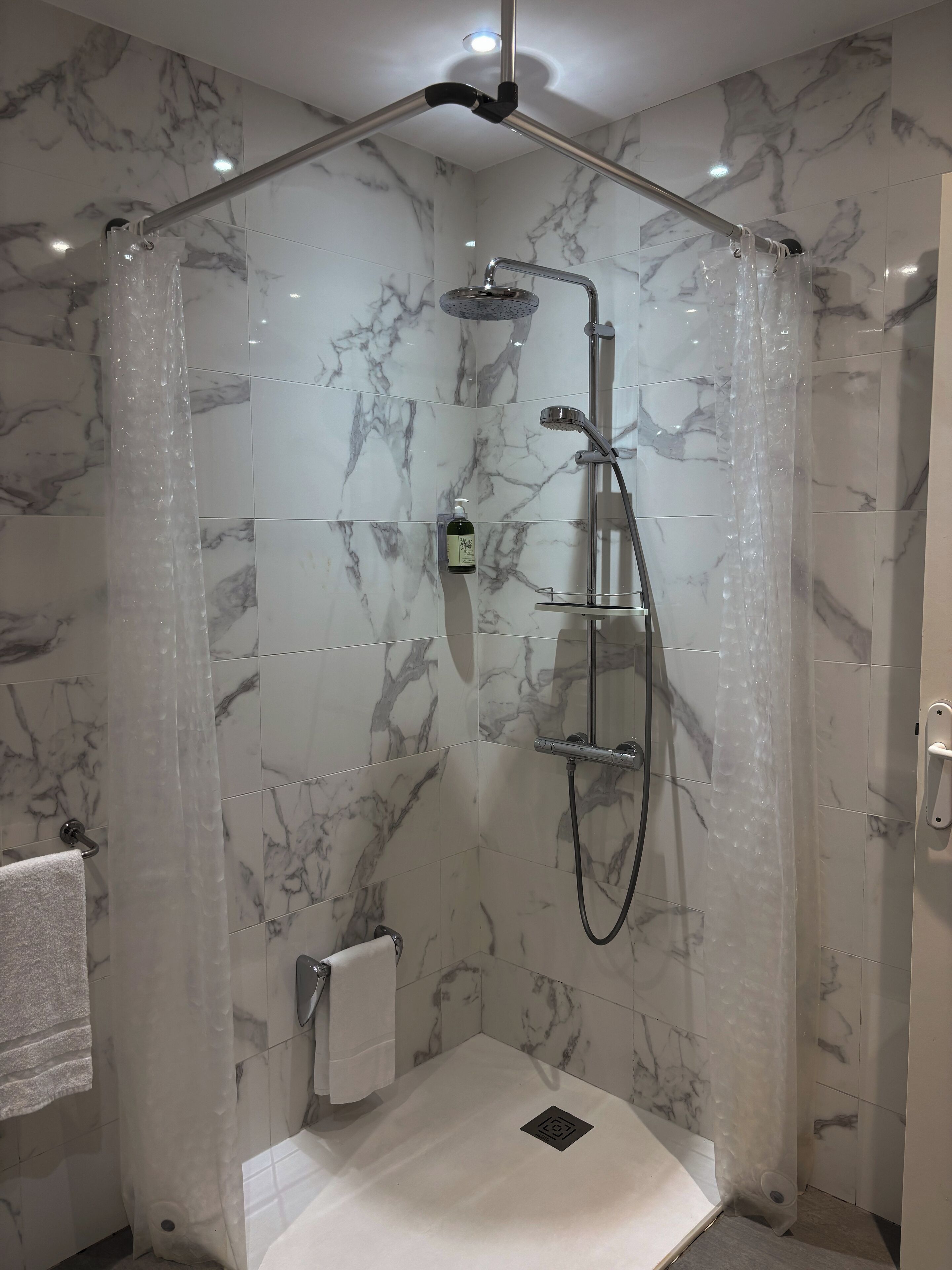 Une douche moderne dotée d’une paroi en verre, d’un pommeau de douche à main et d’un robinet mural.