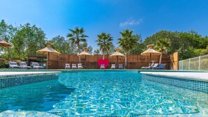 Una piscina con sillas de descanso y sombrillas, rodeada de palmeras y una valla de madera.