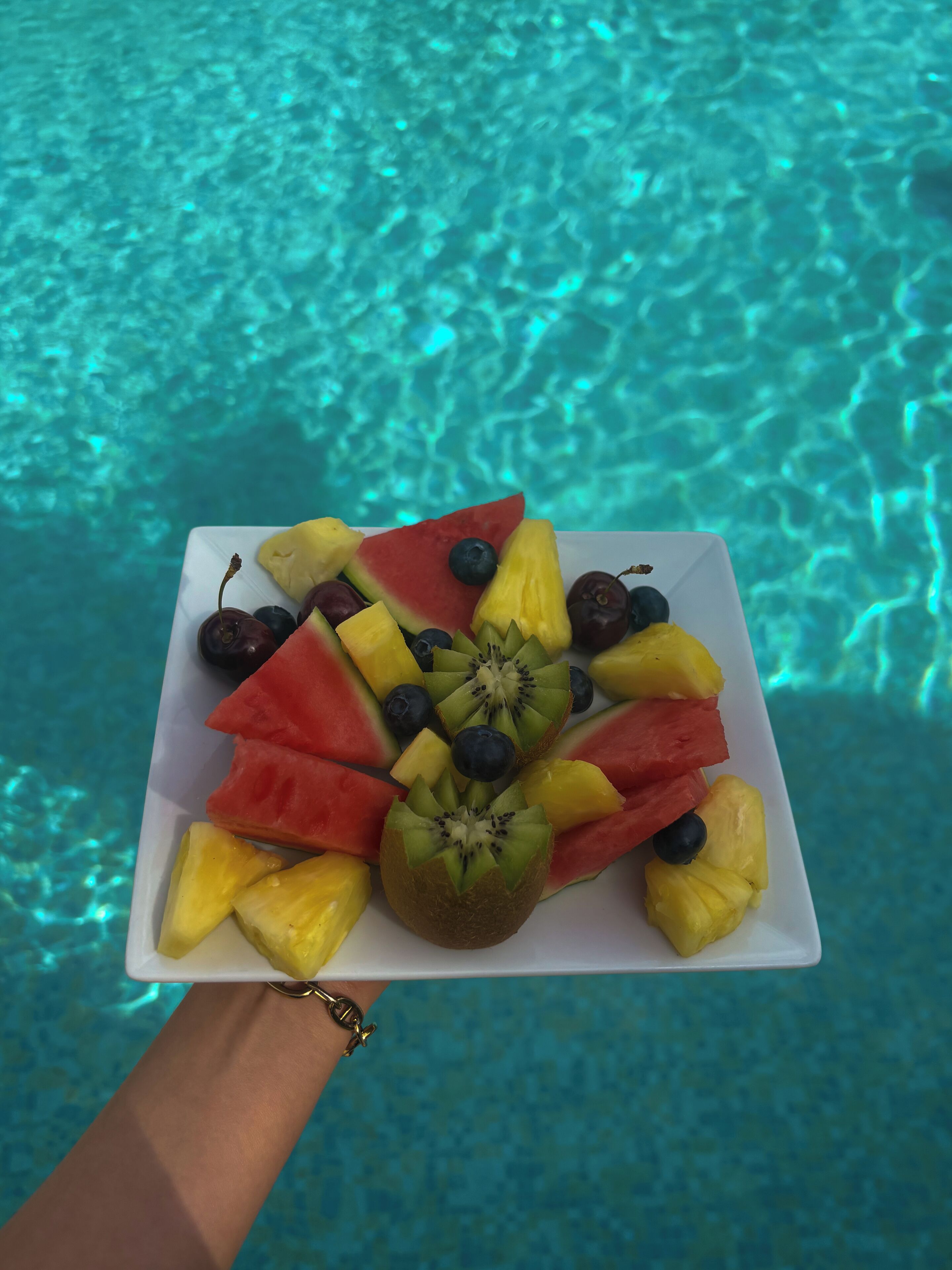 A plate of fruit held over a pool with clear water.
