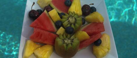 Une assiette de fruits est placée au-dessus d’une piscine dont l’eau est claire.