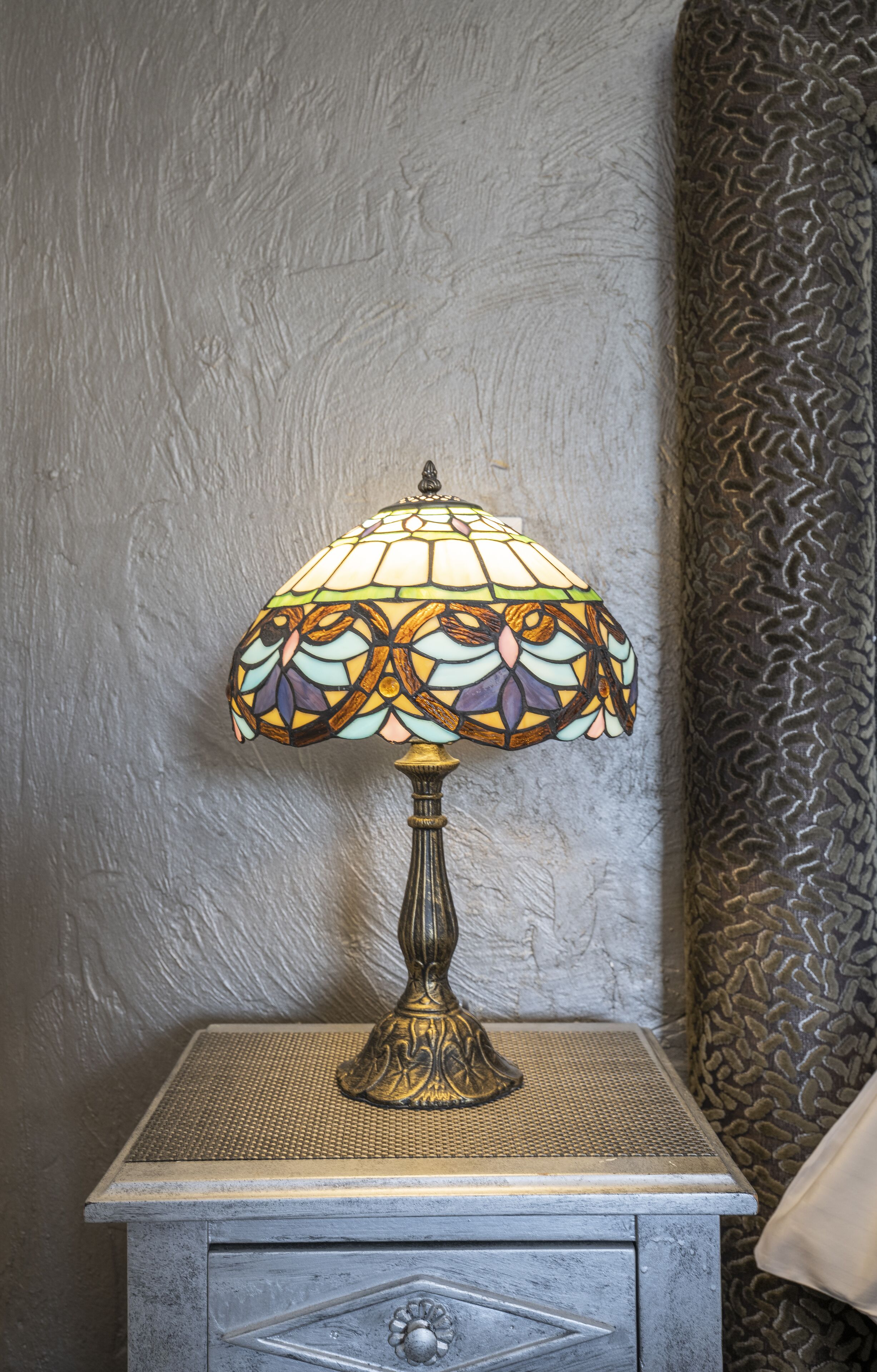 Eine Tischlampe mit einer farbigen Glasschirm an einer strukturierten Wand.