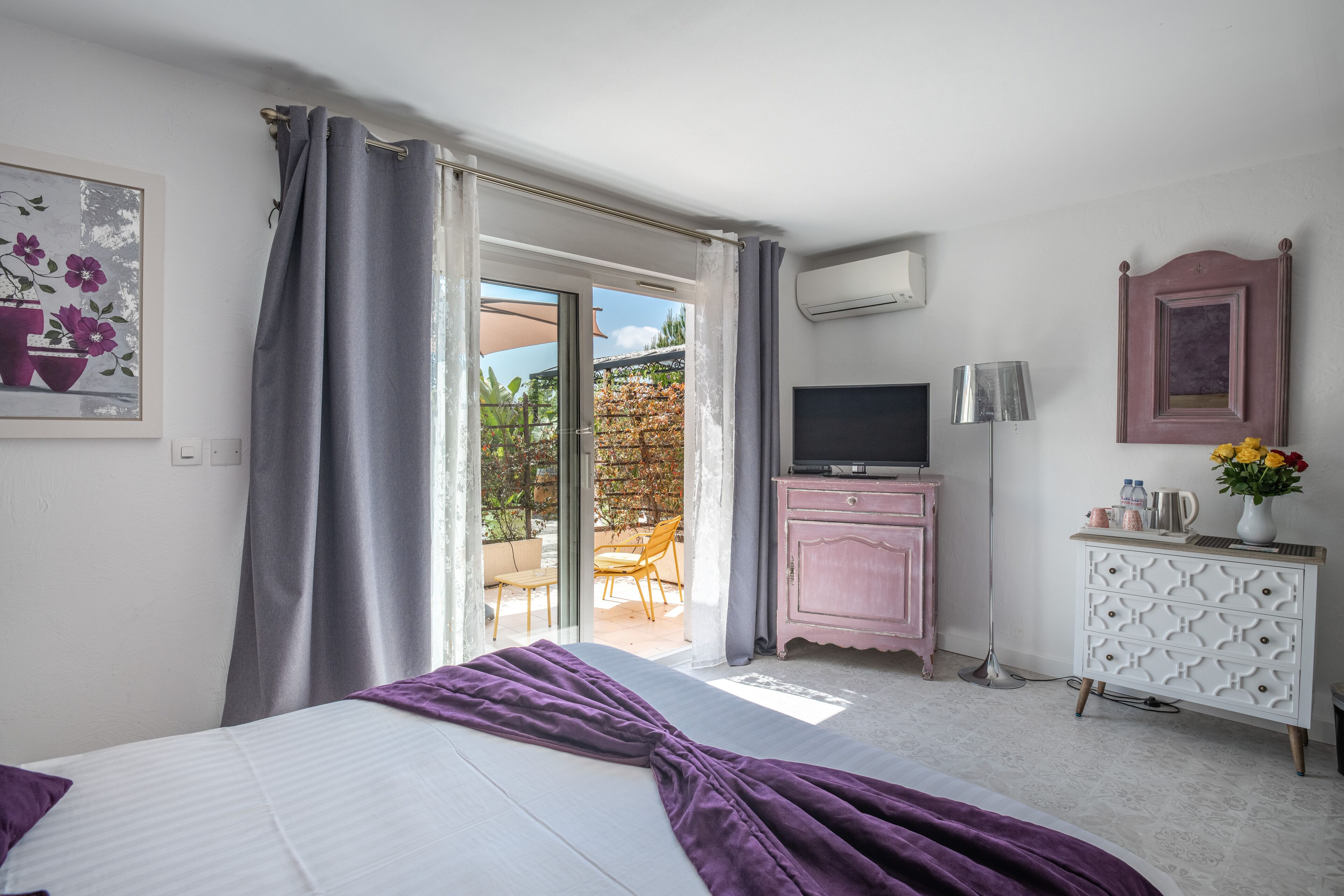A bedroom with a bed, a TV, a dresser, and a balcony with a chair and table.