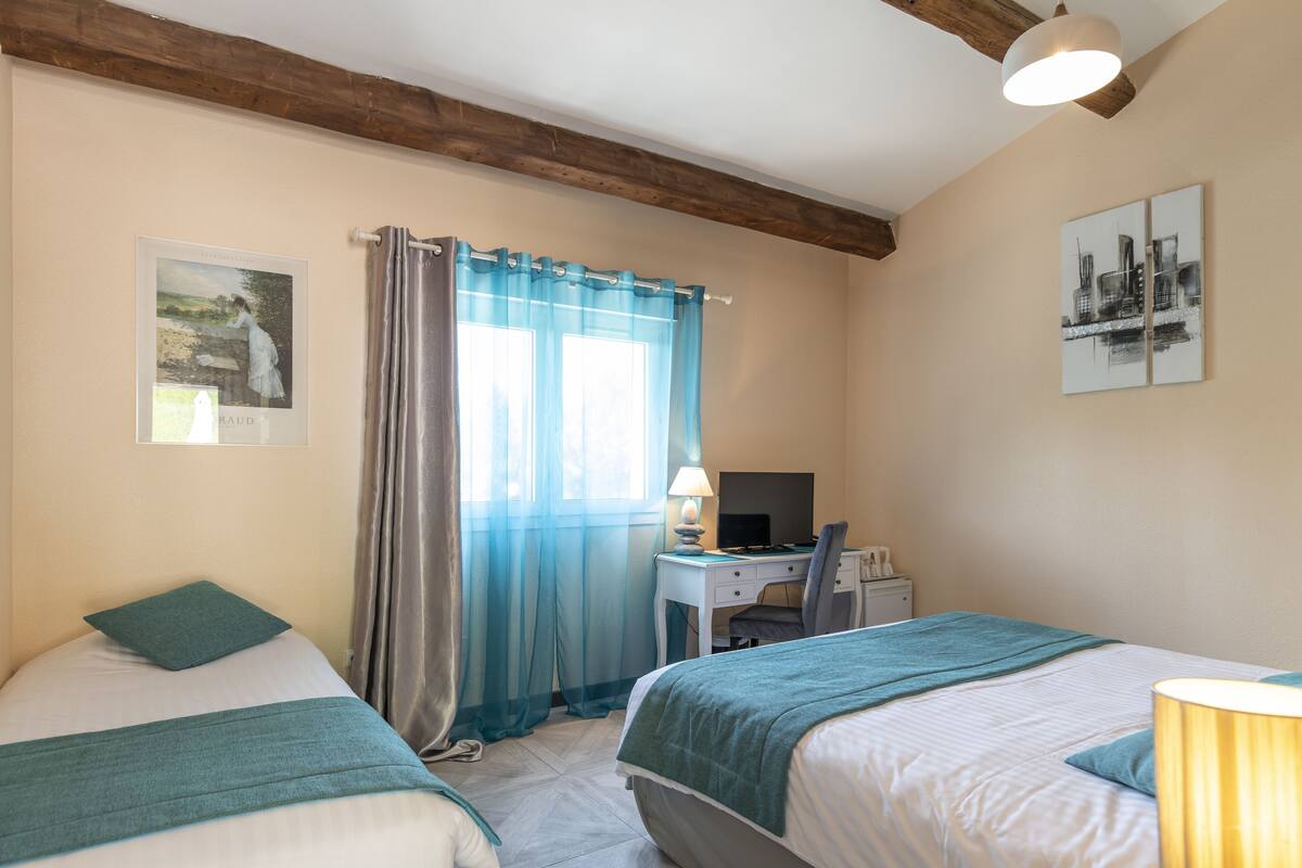 Ein Hotelzimmer mit zwei Betten, einem Schreibtisch mit Computer, einem Stuhl und einer Lampe.