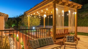 Un espacio al aire libre cubierto con una pérgola de madera, asientos acolchados y una mesa de vidrio.
