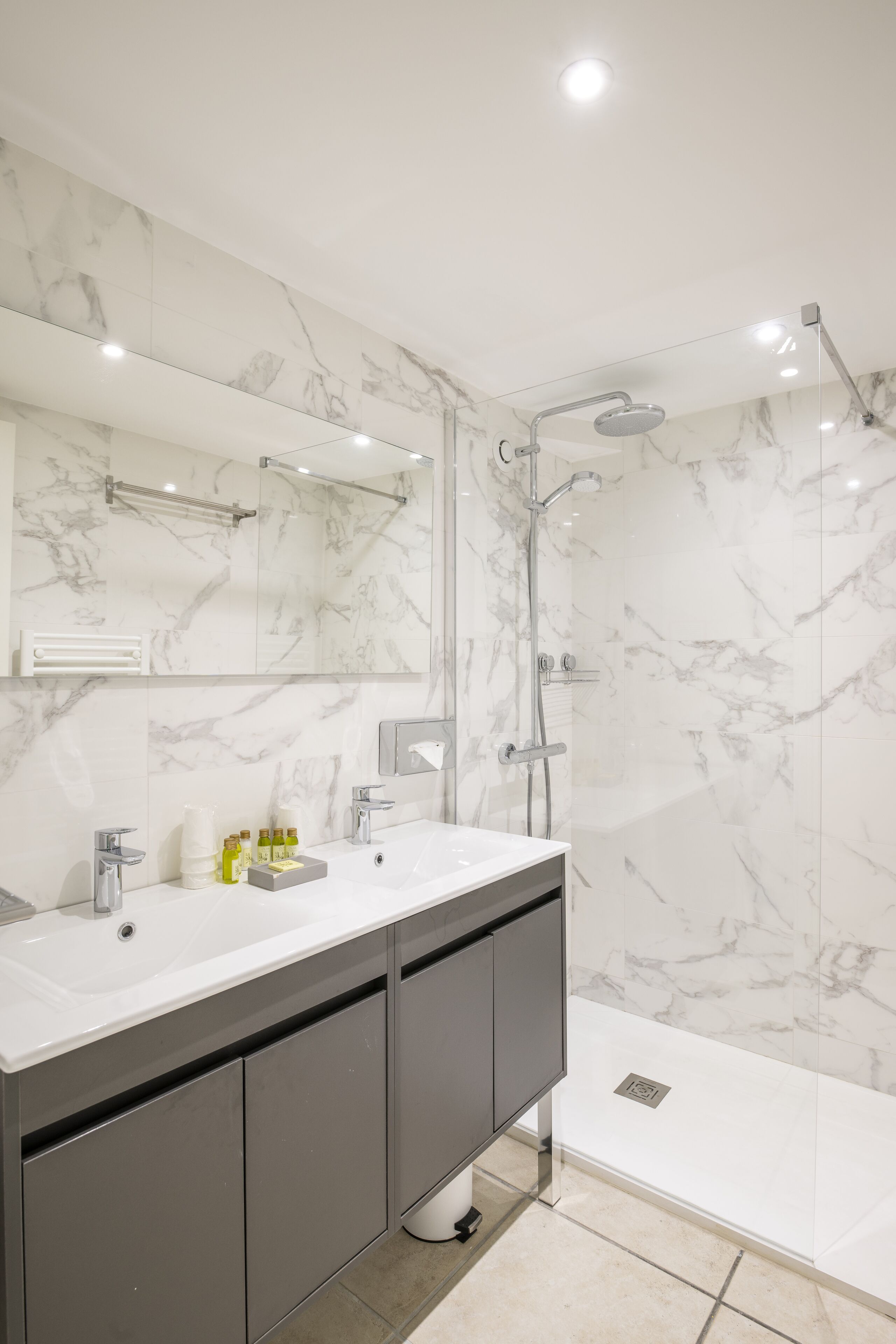 A modern bathroom with a marble backsplash, a dual sink vanity, a glass-enclosed shower, and a built-in toilet.