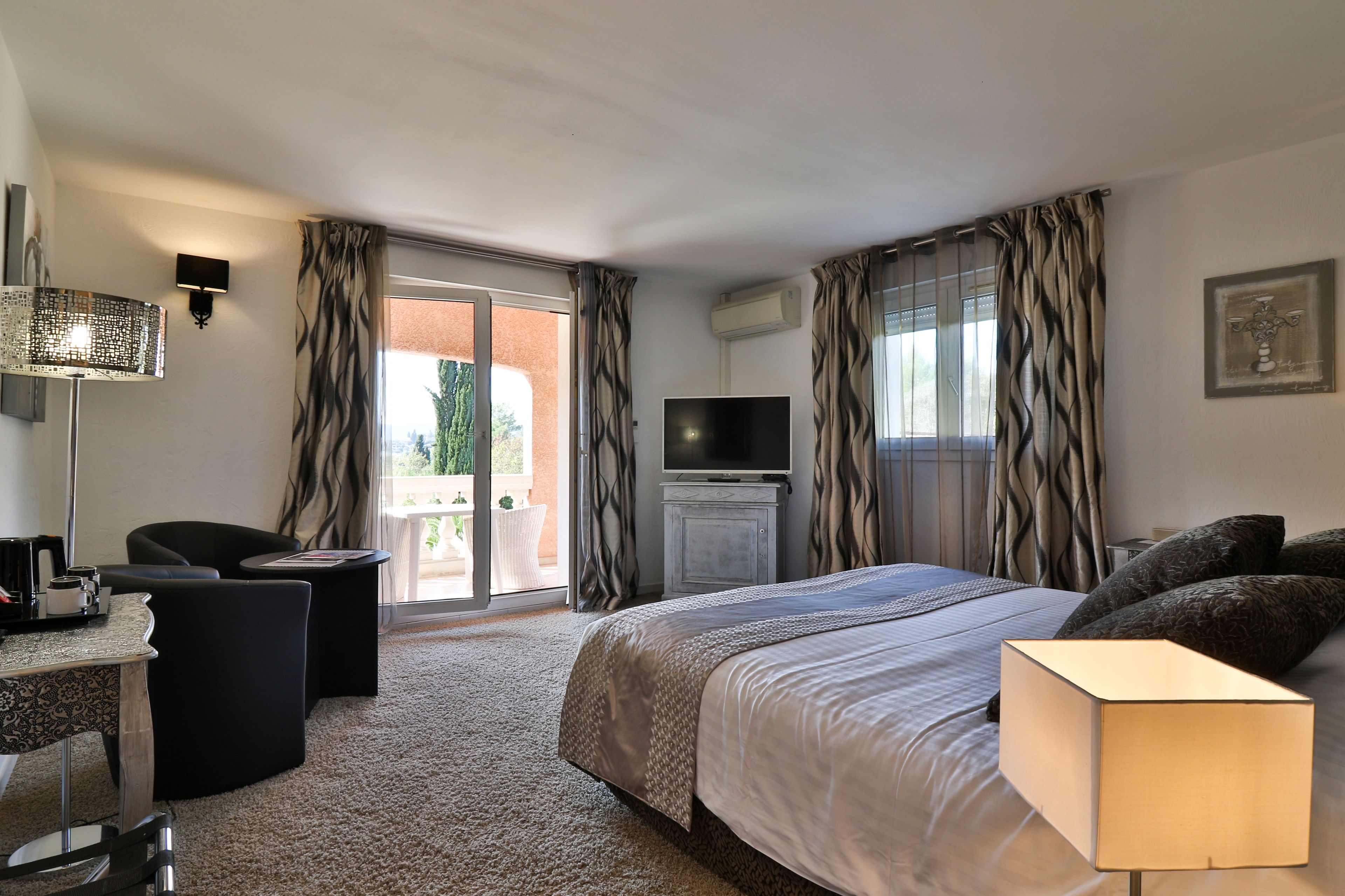 A hotel room with a bed, a desk, a chair, a TV, and a view of the outdoors.
