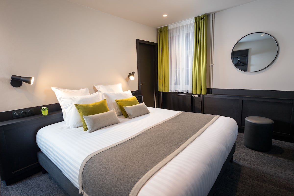 A hotel room with a large bed, bedside tables, a mirror, and a window with curtains.