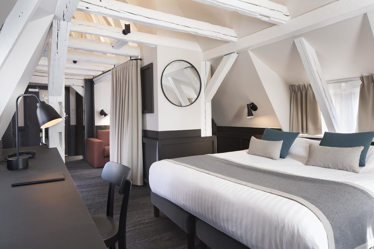 A modern hotel room with a bed, desk, chair, and a round mirror on the wall.