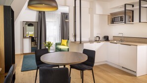 A modern kitchen with a dining area, featuring a round table, chairs, a hanging light fixture, and a built-in microwave. - Hotel Du Dragon (Strasbourg)