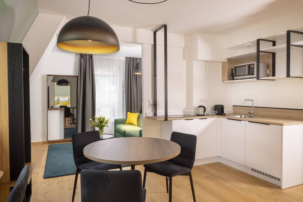 A modern kitchen with a dining area, featuring a round table, chairs, a hanging light fixture, and a built-in microwave.