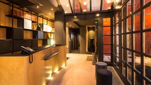 A reception area with a reception desk, a phone, and a seating area with a bench. - Hotel Du Dragon (Strasbourg)