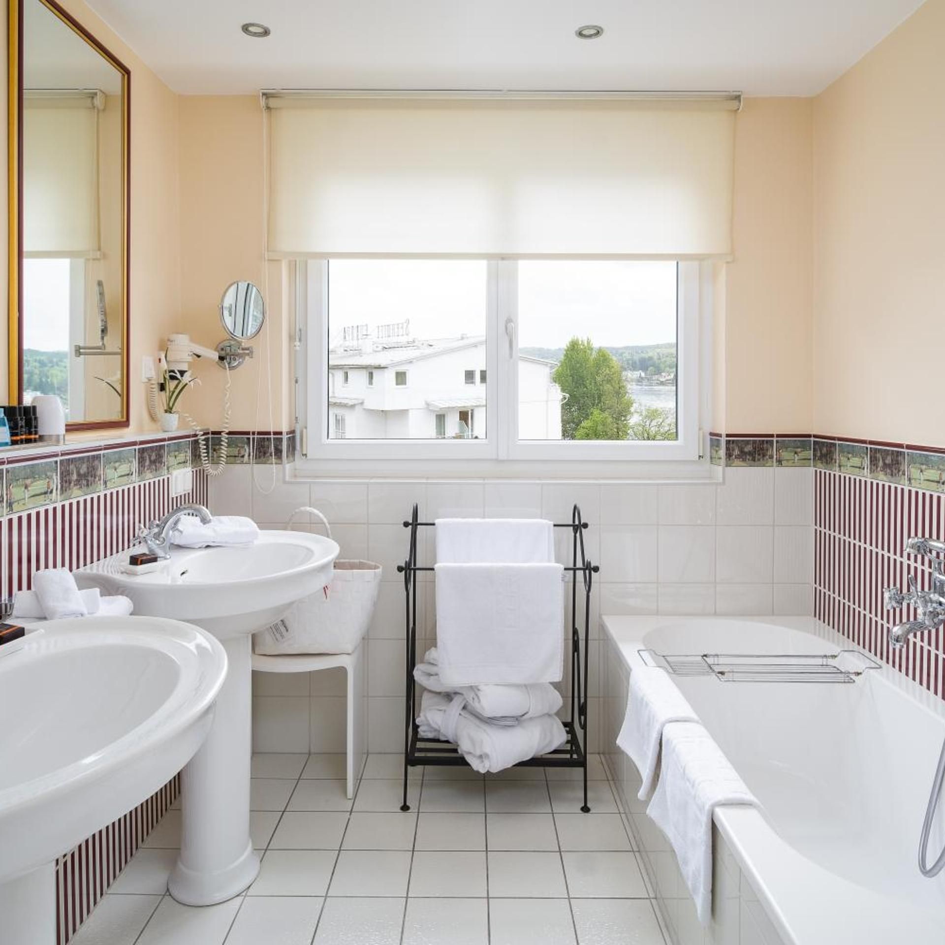 Une salle de bain avec deux lavabos, une baignoire et une fenêtre donnant sur des immeubles.