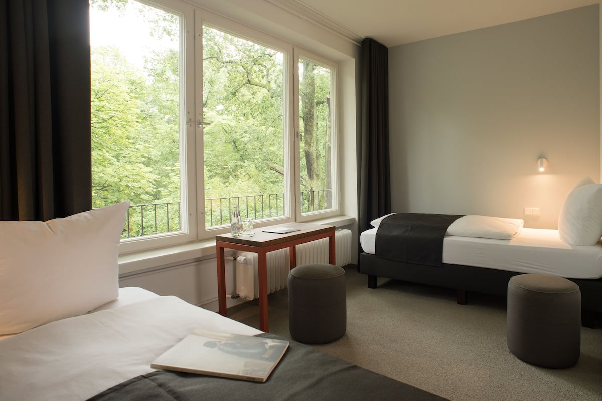A hotel room with a bed, a sofa, a small table, and a window with a view of trees.
