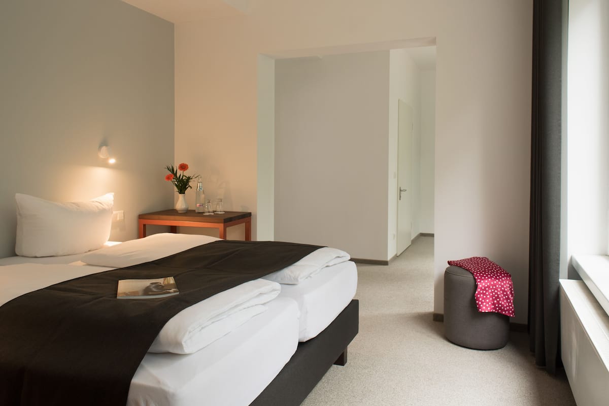 A modern hotel room with a neatly made bed, a bedside table with a vase of flowers, and a window with a view.