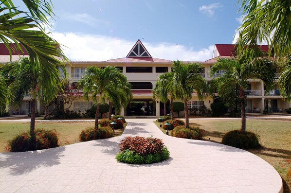 Un hotel con entrada central, rodeado de palmeras y un camino pavimentado.