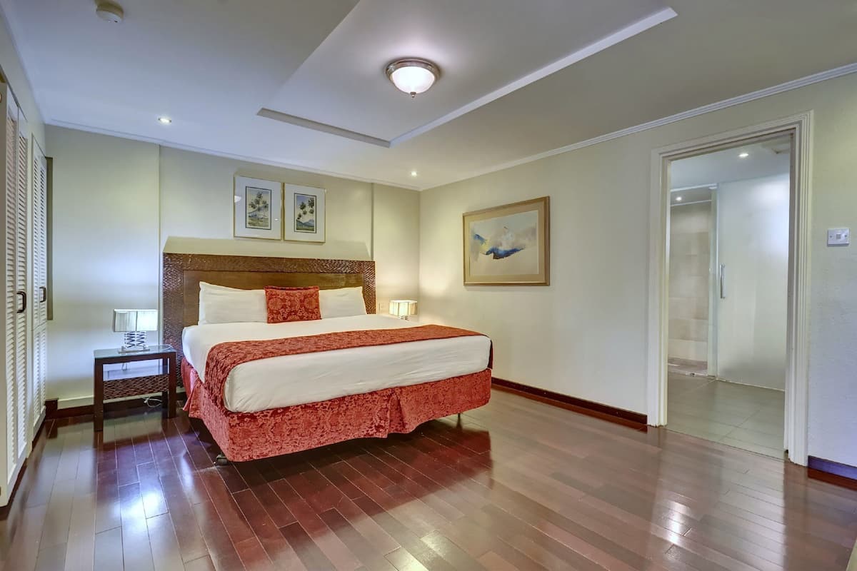 Une chambre d’hôtel avec un grand lit, une table de chevet avec une lampe et une porte donnant sur une autre pièce.