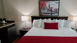 Ein Hotelzimmer mit einem großen Bett, zwei Nachttischen, einem Schreibtisch und einem Kühlschrank.