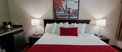 A hotel room with a large bed, two bedside tables, a nightstand, a desk, and a refrigerator.