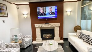 Ein modernes Wohnzimmer mit Kamin, gemusterten Sofas, einem Couchtisch und einem Fernseher, der eine Nachrichtensendung zeigt.