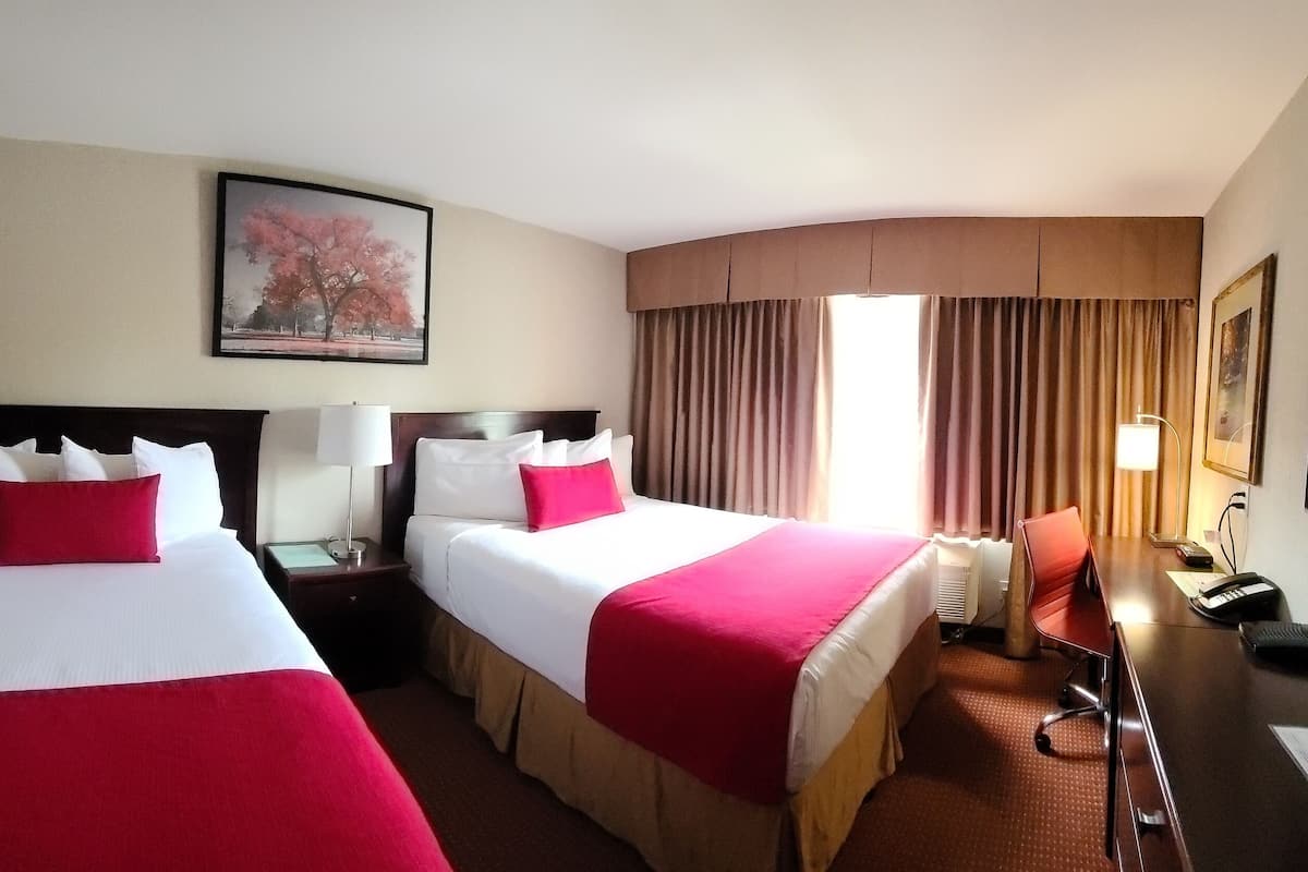 Une chambre d’hôtel avec deux lits, un bureau, une chaise, une télévision et une fenêtre avec des rideaux.