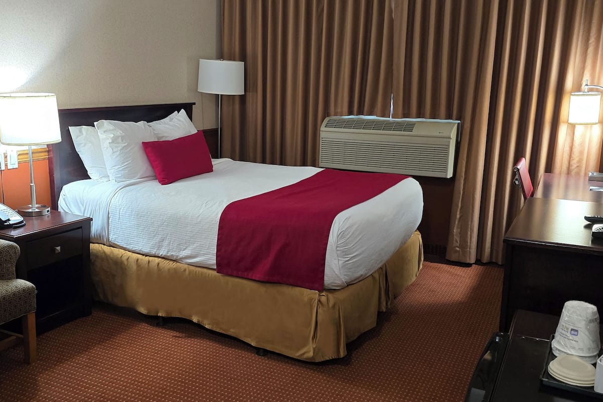 Une chambre d’hôtel équipée d’un lit, d’une chaise, d’un bureau avec une lampe, d’une télévision et d’un mini-bar.