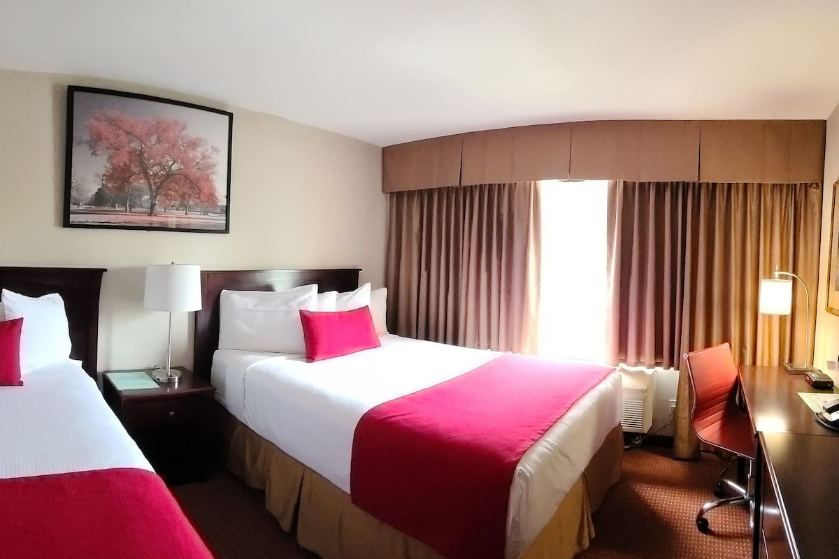 Une chambre d’hôtel avec deux lits, un bureau, une chaise, une lampe et un tableau au mur.