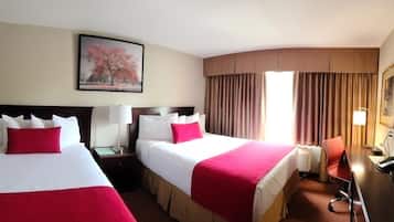 Habitación de hotel con dos camas, un escritorio, una silla, una lámpara y un cuadro en la pared.