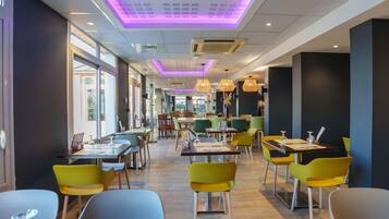 A modern restaurant interior with wooden flooring, yellow and green chairs, and purple ceiling lighting.