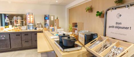 Zona de desayuno tipo buffet con un letrero que dice 'Bon petit déjeuner!' y una cafetera.