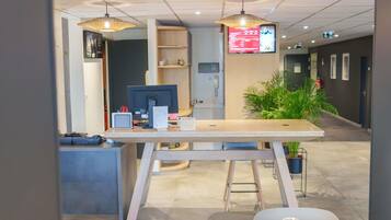 A reception desk with a computer, a plant, and a TV screen.