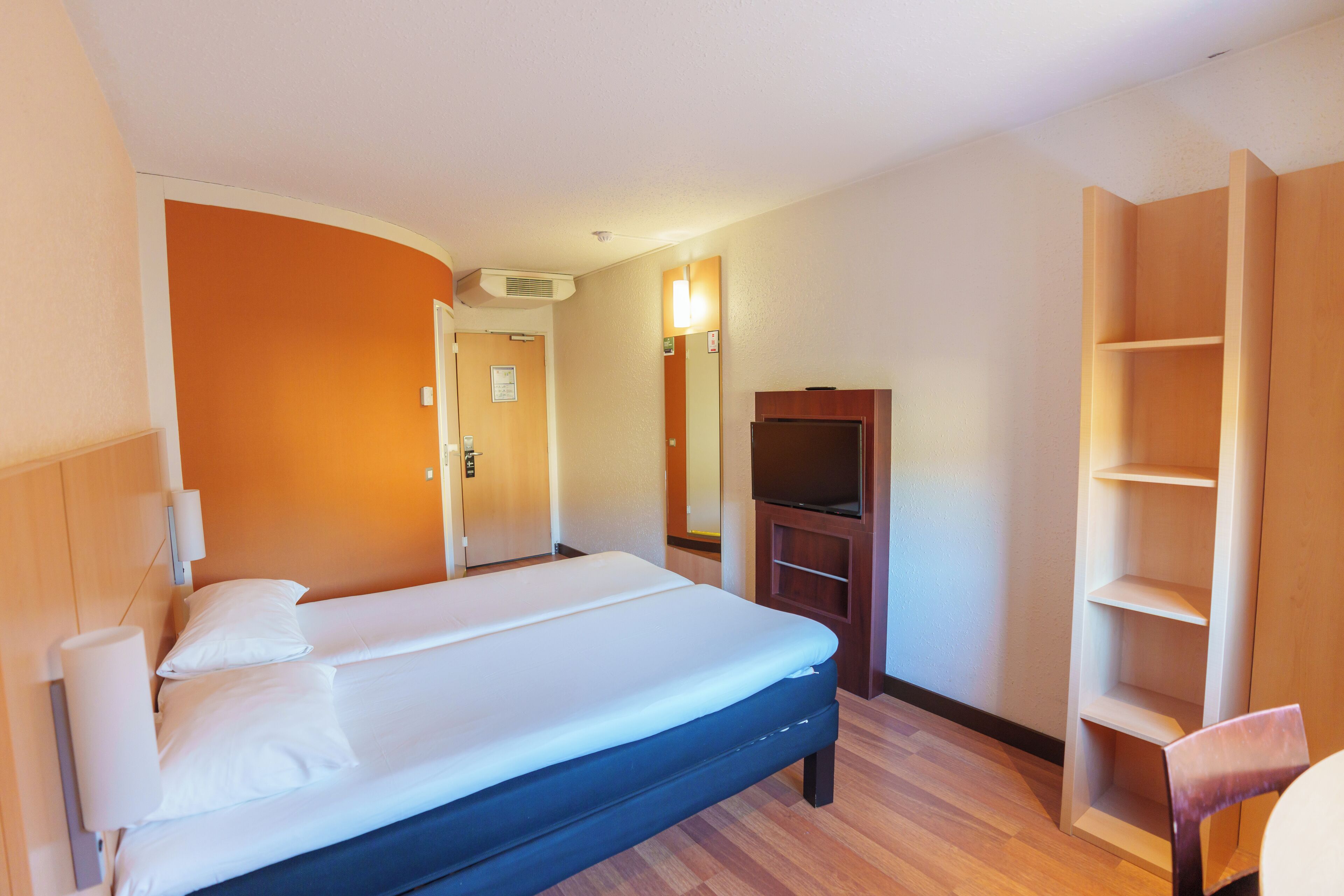 A hotel room with a bed, a TV, a wooden wardrobe, and a chair.
