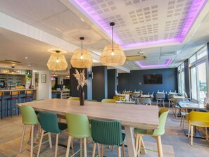 Un comedor moderno con una gran mesa de madera, sillas verdes y amarillas, e iluminación colgante.