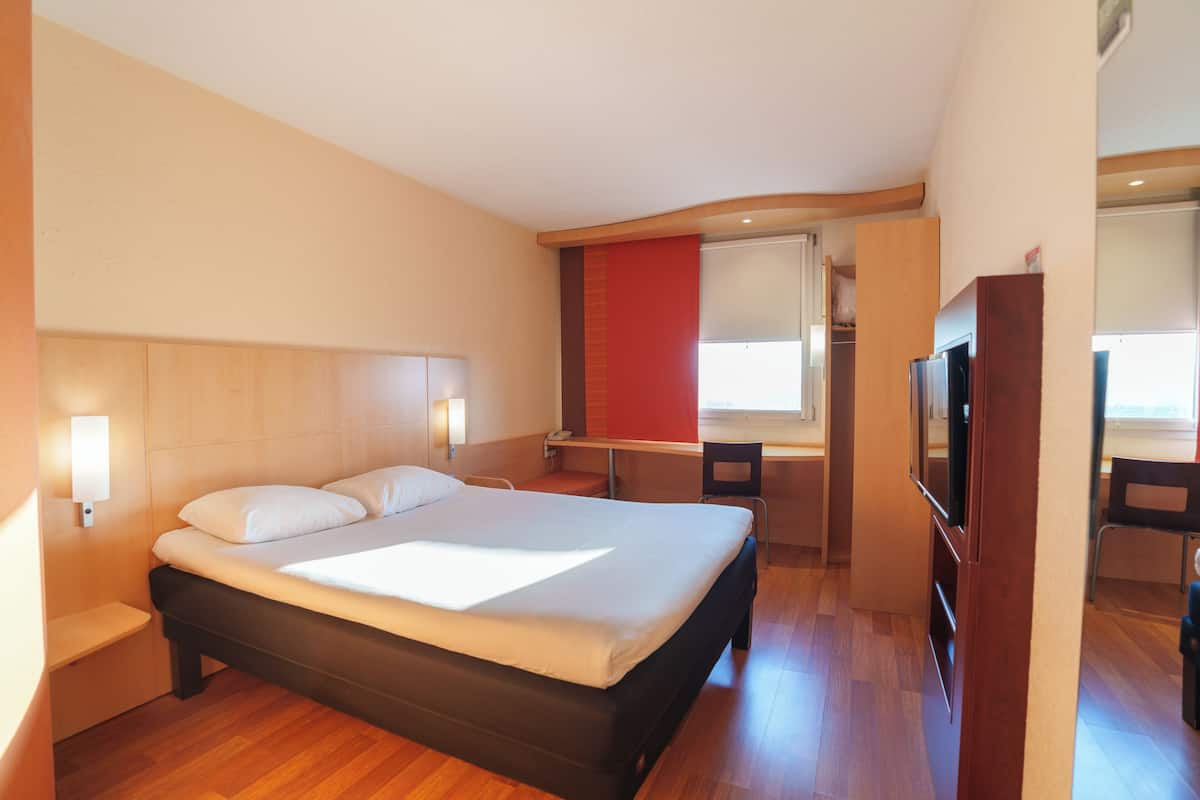 A hotel room with a bed, a desk, a chair, and a TV.